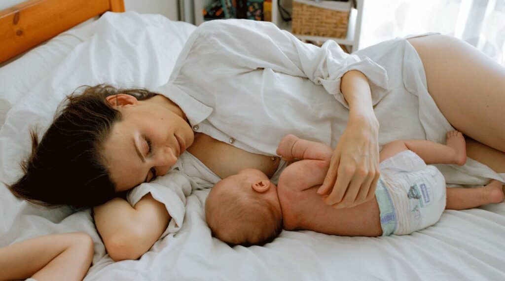 Mother breastfeeding baby outdoors with a light cover