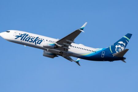 Alaska Airlines plane flying in clear blue sky.